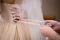 Bride is preparing for ceremony. Hands knotted ribbon on corset