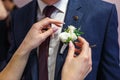 Bride puts groom on boutonniere from pink and whote rose on wedding day