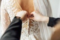 The bride puts on a white lace wedding dress, mom and girlfriend of the bride help to tie the dress from the back. Royalty Free Stock Photo