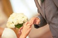 The bride is putting the ring on the groom`s finger and holding the bride`s bouquet in her hand. Royalty Free Stock Photo