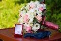 Bride`s wedding bouquet of white and pink flowers. Blue bow tie next to gold wedding rings in a red box. White and pink roses. Royalty Free Stock Photo