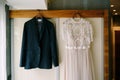 The bride`s wedding dress and the groom`s jacket on wooden hangers, hang on the wardrobe. Royalty Free Stock Photo
