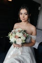 The bride sits on the bed in a dress, holding a bouquet and looking at the camera Royalty Free Stock Photo