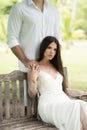 The bride sits on a bench, while the groom stands behind and holds her by the shoulders Royalty Free Stock Photo