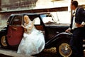 Bride sits in an open door of a retro car while groom waits behind it