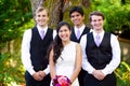 Bride standing with her three groomsmen outdoors under large tre