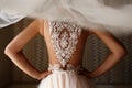 The bride stands with her back to the camera. Veil and lace on the back of a girl. Woman holds hands on a belt