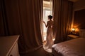 Bride stands near the window in the hotel