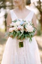 A bride stands in an olive grove and holds in her hands a bouquet with roses, peonies, lisianthus and eucalyptus, close Royalty Free Stock Photo