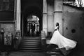 Bride stands on the stones spreading her dress while groom walks