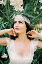 Bride straightens her hair near a blooming white oleander bush