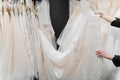 Bride touches luxurious white cream wedding dress on hangers. Dresses made of silk chiffon, tulle and lace. Royalty Free Stock Photo