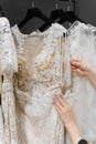 Bride touches luxurious white cream wedding dress on hangers. Dresses made of silk chiffon, tulle and lace. Royalty Free Stock Photo