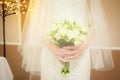 the bride in a veil and a white dress holds a bouquet with flowers in her hands on wedding ceremony. Close-up, indoor Royalty Free Stock Photo