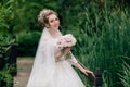 The bride is walking along the bridge over the river. The girl is posing in a wedding dress and a bouquet of peonies in Royalty Free Stock Photo