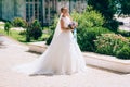 The bride is wearing a curvy dress and walks with a long veil along the picturesque avenue. Wedding walk with a bouquet Royalty Free Stock Photo