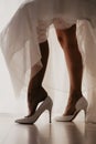 Bride wearing high heel shoe on mirror floor near panoramic window on wedding day. Bride putting her elegant leg into white shoe Royalty Free Stock Photo