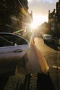 A bride wearing a wedding dress standing in front of a car in the sunshine Royalty Free Stock Photo