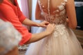 The bride wears a wedding dress, mom and girlfriend of the bride help to tie the dress from the back Royalty Free Stock Photo