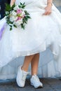 Bride with a wedding bouquet dressed in white dress showing sneakers on her legs