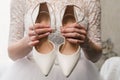 The bride in a wedding dress holds white shoes in well-groomed hands with a beautiful manicure Royalty Free Stock Photo