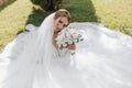 a bride in a wedding dress with a long train and a veil holds a wedding bouquet of roses while sitting under a veil Royalty Free Stock Photo