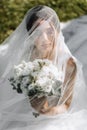 a bride in a wedding dress with a long train and a veil holds a wedding bouquet of roses while sitting under a veil Royalty Free Stock Photo