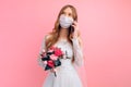 Bride in a wedding dress with a medical protective mask on her face, talking on a mobile phone on a pink background. Quarantine, Royalty Free Stock Photo