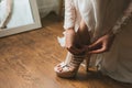 The bride in a wedding dress on morning preparation dresses beautiful beige shoes sandals close-up. Wooden background Royalty Free Stock Photo