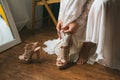 The bride in a wedding dress on morning preparation dresses beautiful beige shoes sandals close-up. Wooden background Royalty Free Stock Photo