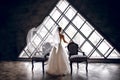 The bride in a white wedding dress stands near two striped armchairs, against the background of a triangular design window Royalty Free Stock Photo