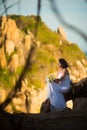 Bride in the wedding dress sits against the Asian mountains at sunset
