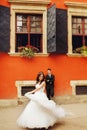 Bride whirls before a groom standing behind an orange house