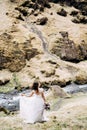 A bride in a white dress and a bouquet of flowers in her hands walks along the banks of a mountain river, near Royalty Free Stock Photo