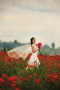 Bride in a white dress with bouquet of red poppies, warm sunset time on the background of the big red poppy field. Copy space. The Royalty Free Stock Photo