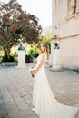 Bride in a white dress with a bouquet stands near an ancient building with sculptures