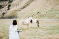 Bride in a white dress goes to the horses in the pasture. Back view Royalty Free Stock Photo