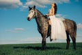 Bride in white dress sits horseback on dapple grey horse Royalty Free Stock Photo