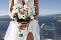 Bride in a white dress with a slit holds bouquet on background of sea and sky