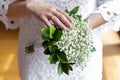 Bride in a white dress standing and holding a wedding bouquet of white gypsophila, close up.