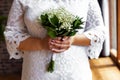 Bride in a white dress standing and holding a wedding bouquet of white gypsophila, close up.