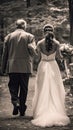 Bride in a white dress walking arm-in-arm with an older man in a suit along a wooded path, symbolizing a father-daughter moment Royalty Free Stock Photo