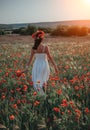 Bride in a white dress in a wreath of red poppies, warm sunset time on the background of the big red poppy field. Copy space. The Royalty Free Stock Photo