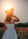 Bride in a white dress in a wreath of red poppies, warm sunset time on the background of the big red poppy field. Copy space. The Royalty Free Stock Photo