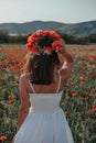 Bride in a white dress in a wreath of red poppies, warm sunset time on the background of the big red poppy field. Copy space. The Royalty Free Stock Photo