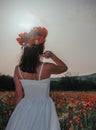 Bride in a white dress in a wreath of red poppies, warm sunset time on the background of the big red poppy field. Copy space. The Royalty Free Stock Photo