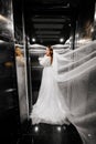 bride in a white elegant dress, with a long veil stands in a dark lift.