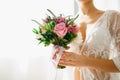 A bride in a white lace peignoir holds a wedding bouquet in her hands in a hotel room while preparing for a wedding