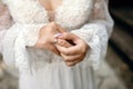 A bride in a white wedding dress and a beautiful manicure holds a gold wedding ring with a diamond with her fingers Royalty Free Stock Photo