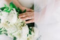 Bride in White Wedding Dress with White Roses Bouquet with Green Leaves, Hand on Flowers with Wedding Ring